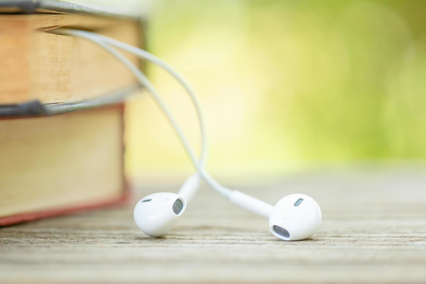 Book and white earphone on wooden table with abstract green nature blur background. Reading and education concept photo