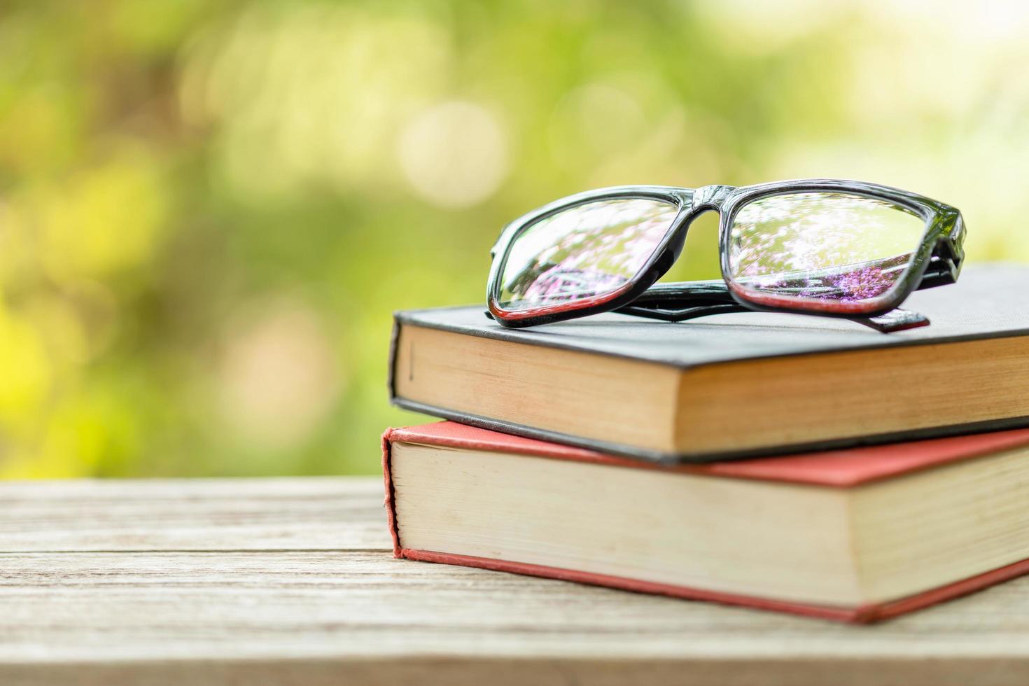 Book and eye glasses on wooden table with abstract green nature blur background. Reading and education concept photo