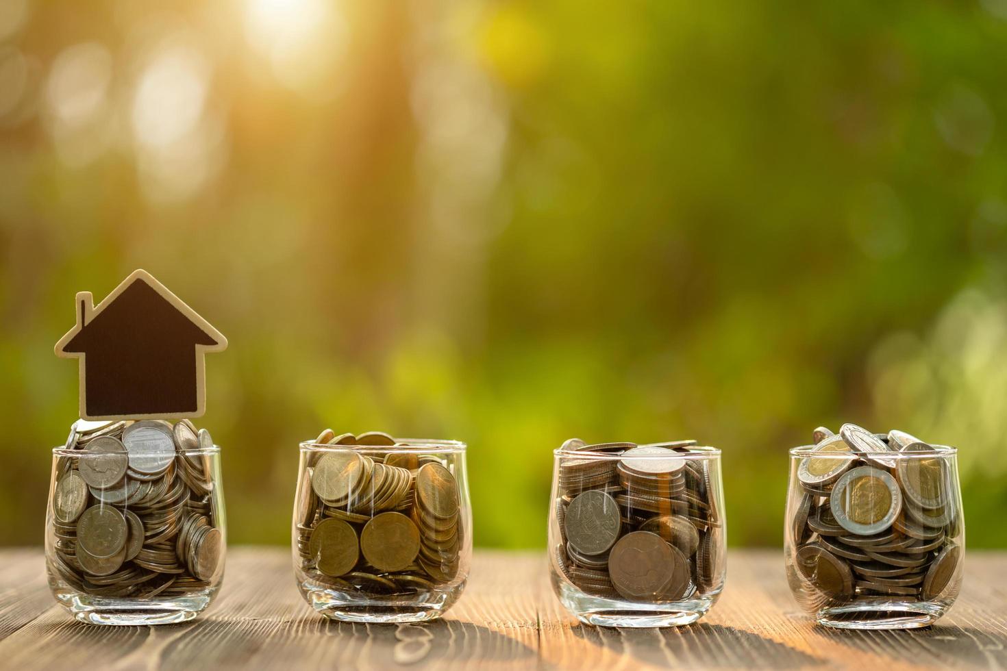 Wooden house model and coin in clear jar on wooden table. Money savings for the home concept photo