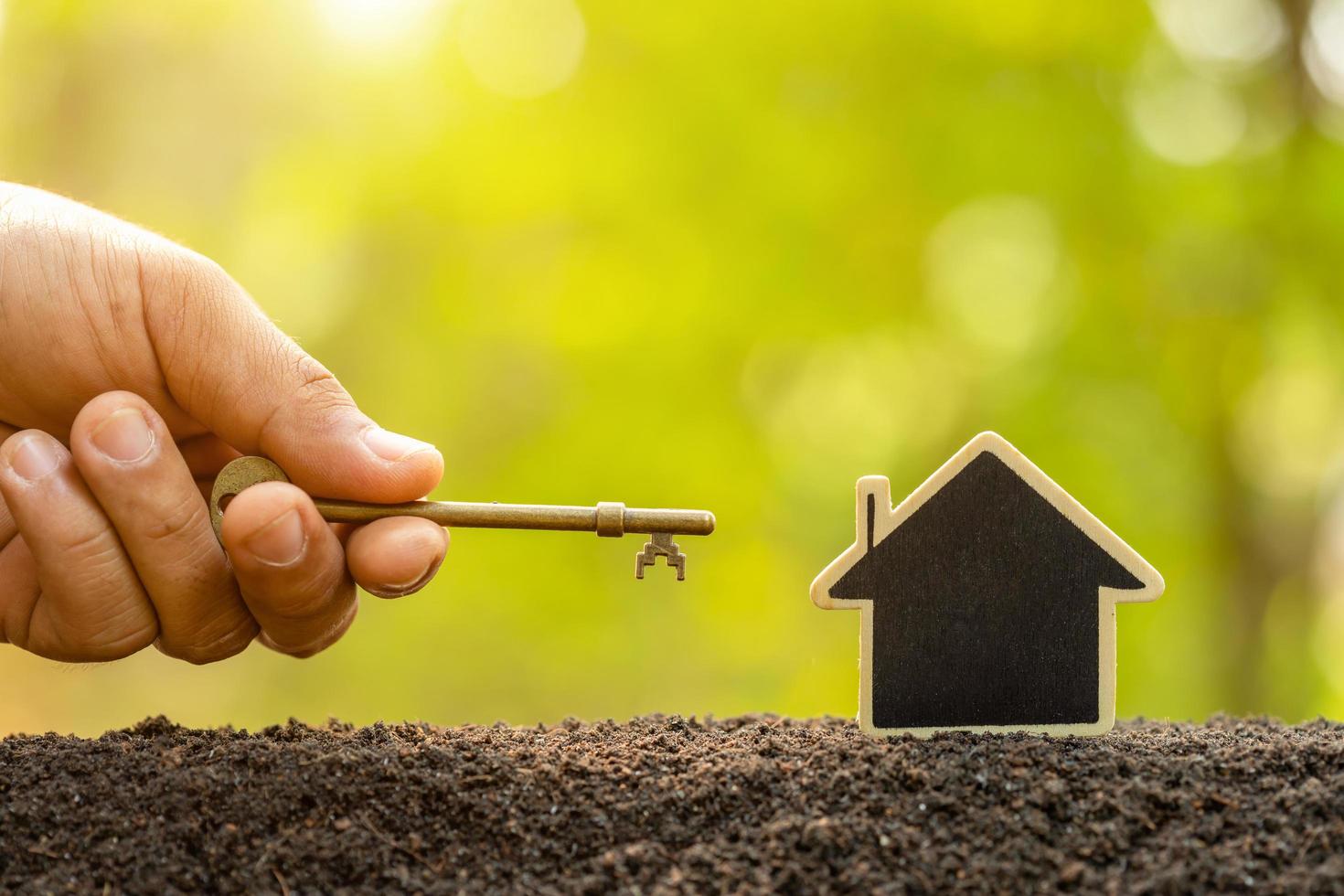 Wooden house growing in soil and vintage key on green nature blur background. Key to success about home business grow up concept photo