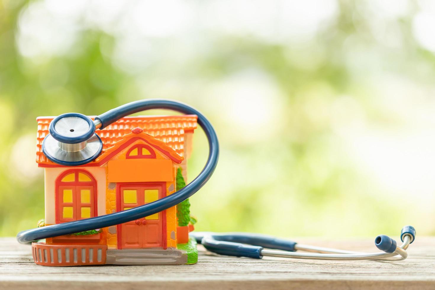 Hand holding blue stethoscope and orange house model on wooden table. Home and building checking photo