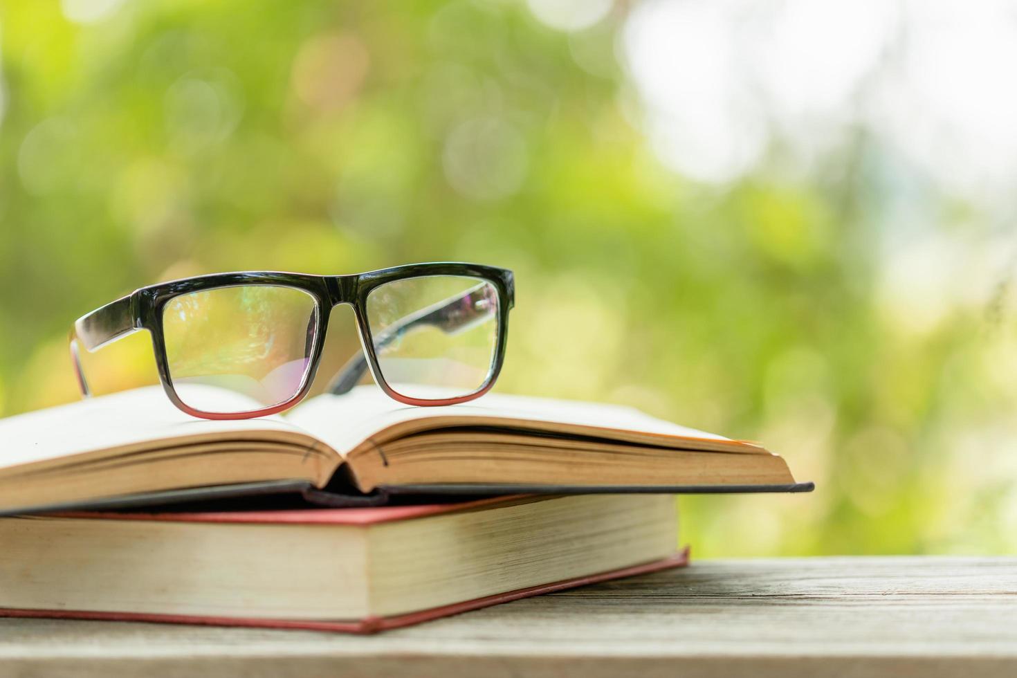 libro y anteojos sobre una mesa de madera con un fondo desenfocado de naturaleza verde abstracta. concepto de lectura y educación foto