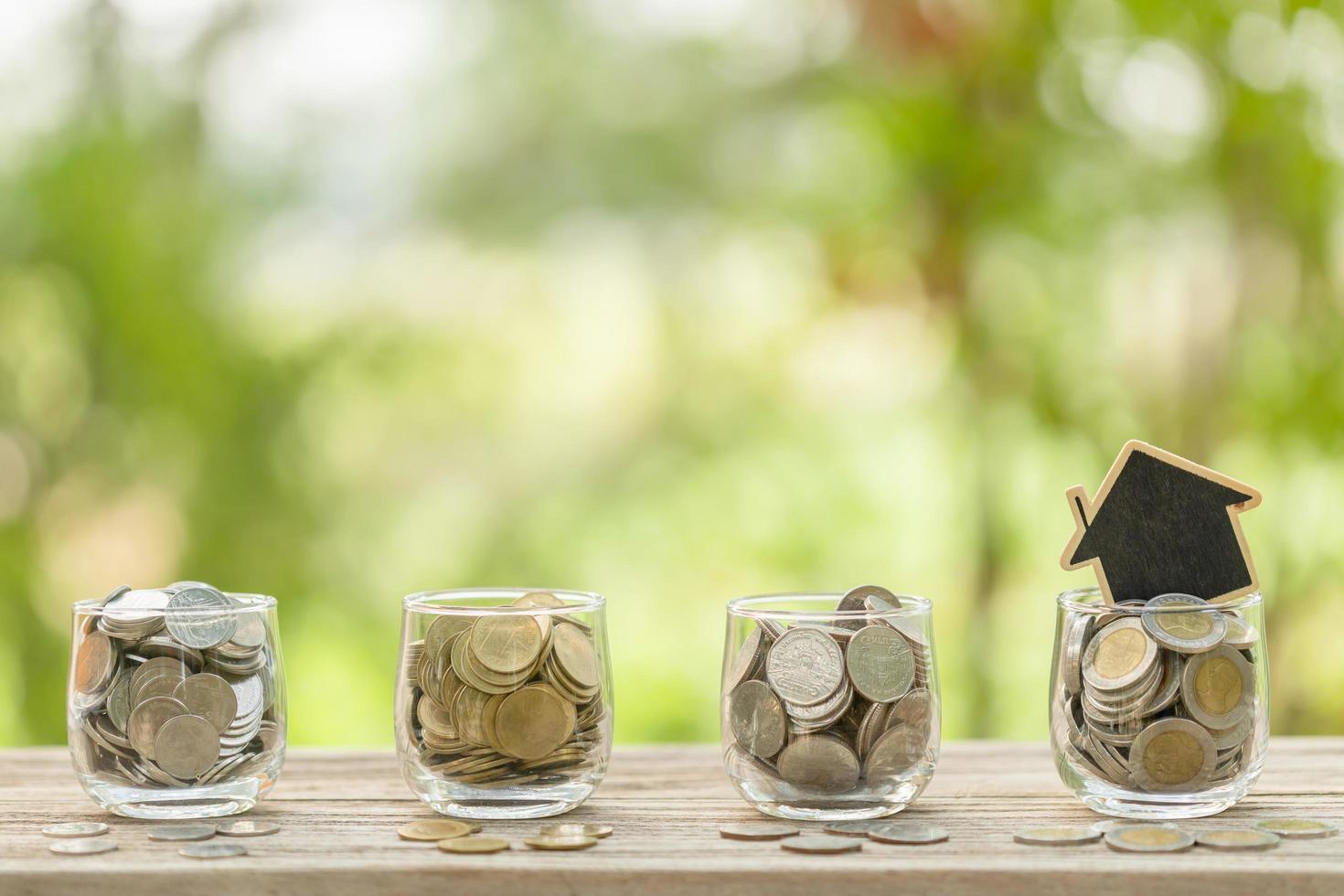 Wooden house model and coin in clear jar on wooden table. Money savings for the home concept photo