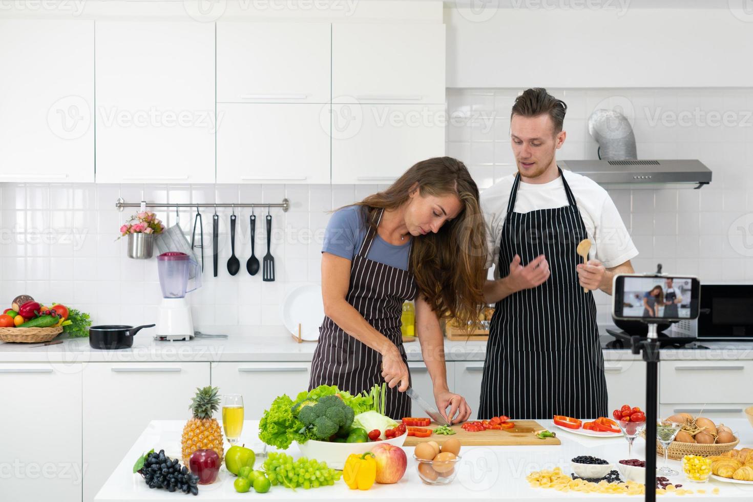 pareja joven transmite enseñando a cocinar comida en la cocina foto