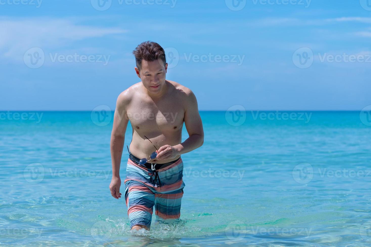 Portrait of Mature Asian Man Walking From Sea to Beach photo