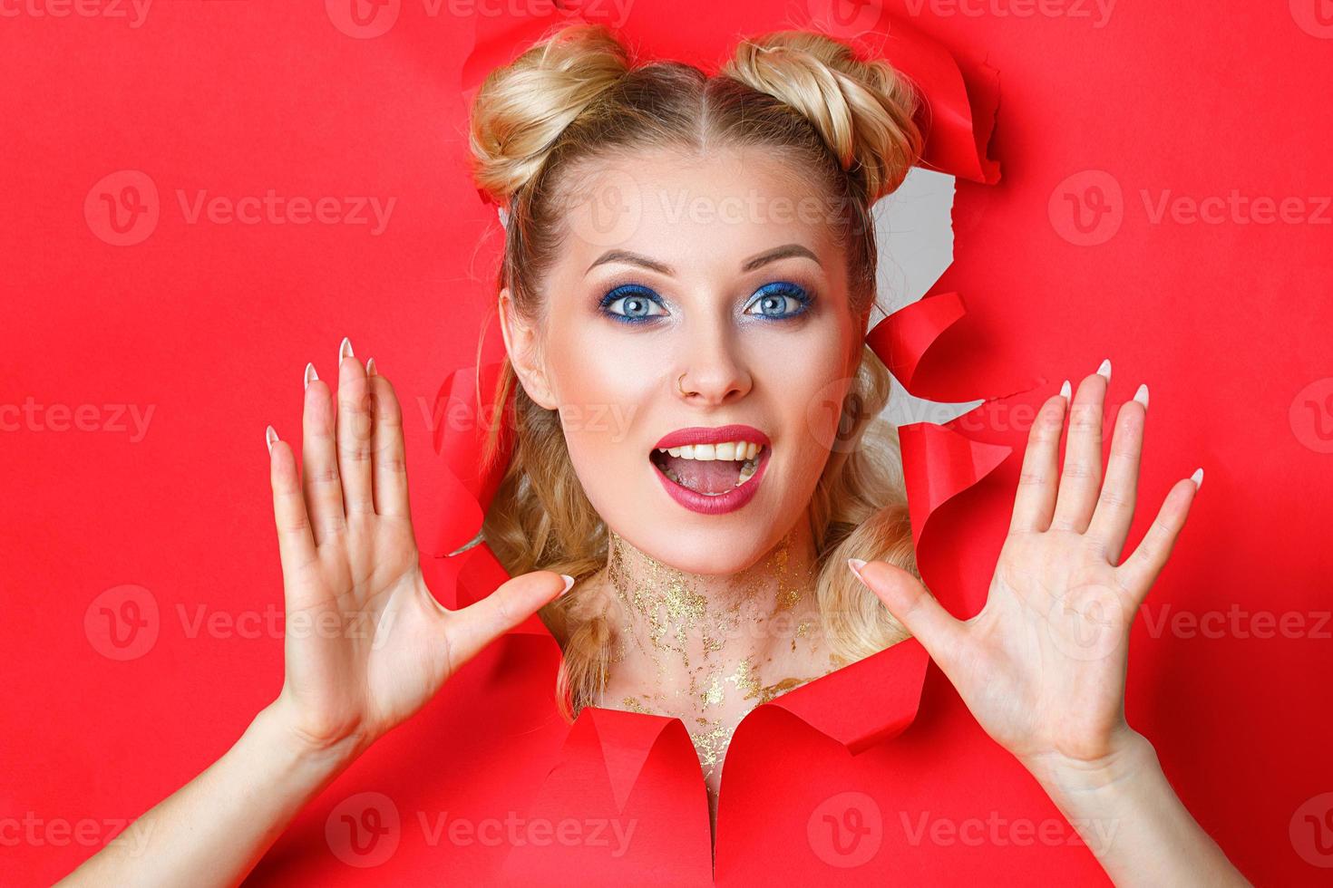 beautiful girl in Peeps out of the hole in red paper, beautiful bright make-up, facial expressions of surprise and interest. photo