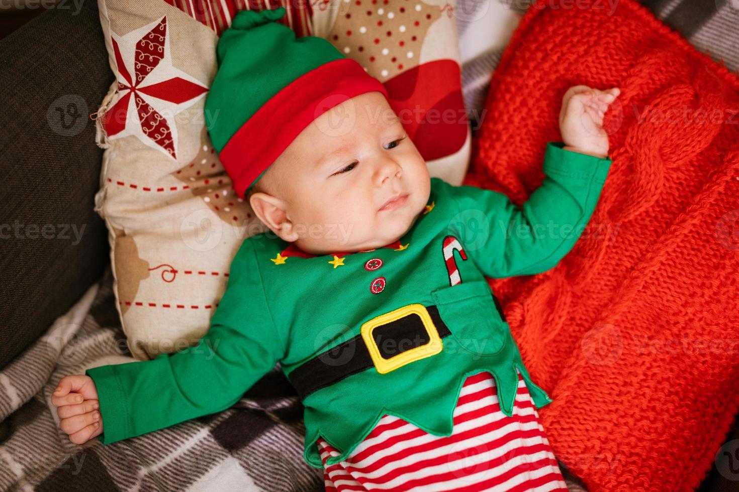 Beautiful half-year-old child lies on pillows and smiles in a red-green costume photo