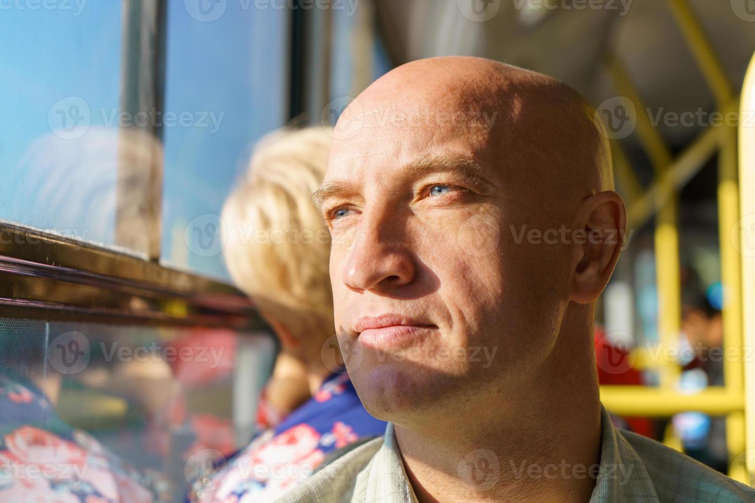 Bald caucasian man rides in public transport while sitting by the window photo