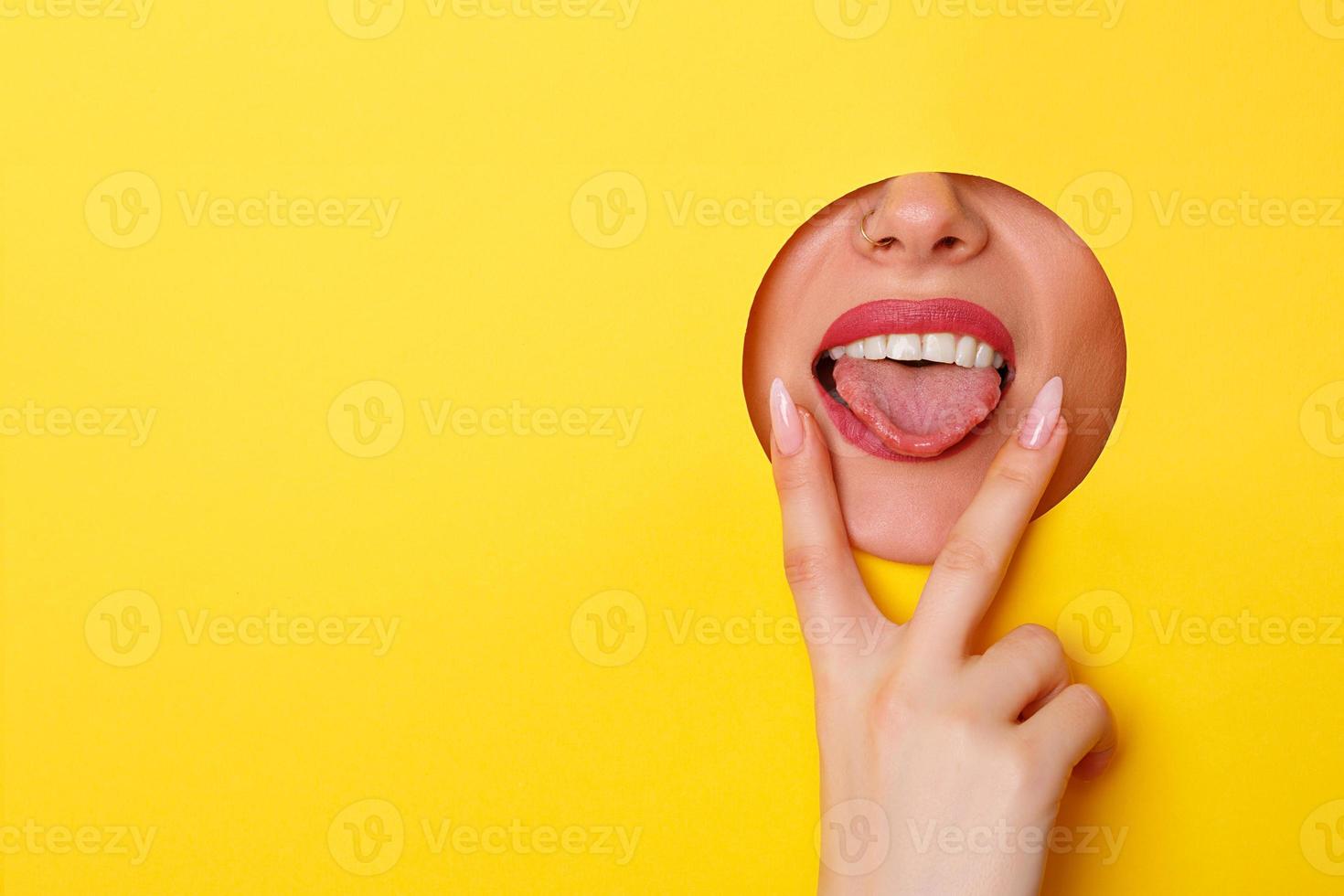 Woman looking in the hole, bright beautiful makeup, big eyes and lips, bright lipstick, professional cosmetics and facial care. Bright colored background and a gap slot in the paper photo