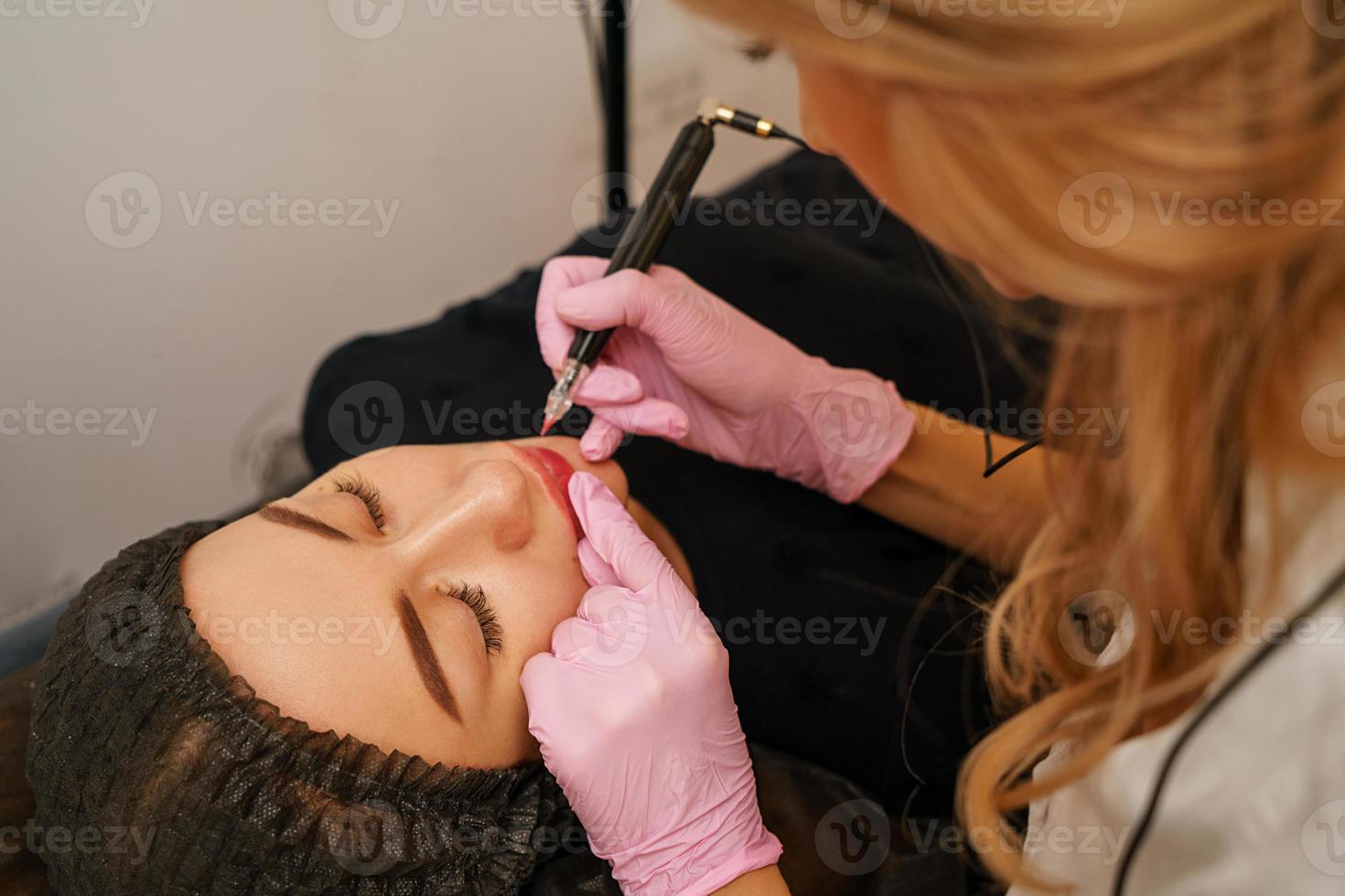 tattoo master makes the client tattoo eyebrows and lips photo
