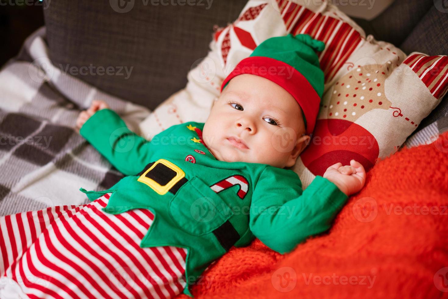 hermoso niño de medio año yace sobre almohadas y sonríe con un traje rojo-verde foto