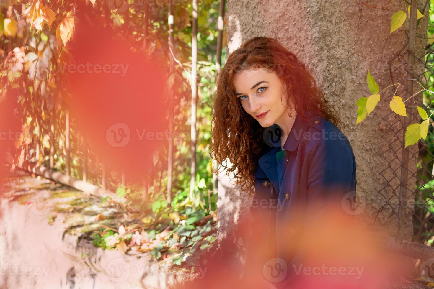 young woman with red hair poses in the street through yellow leaves, photo