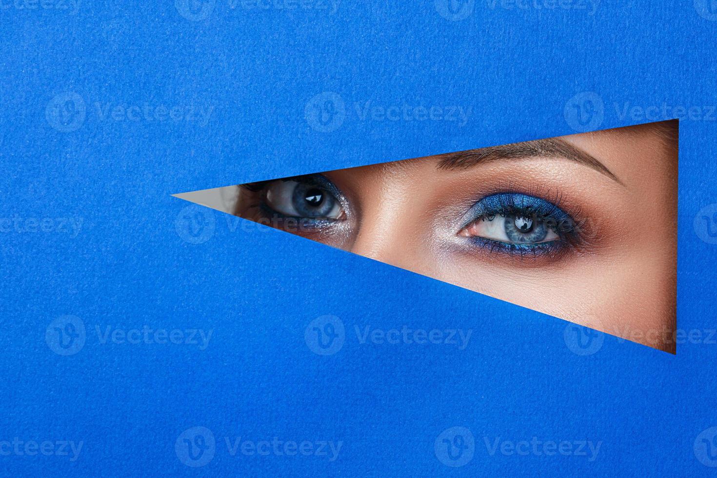 beautiful young woman in a hole in blue paper, beautiful bright make-up. photo