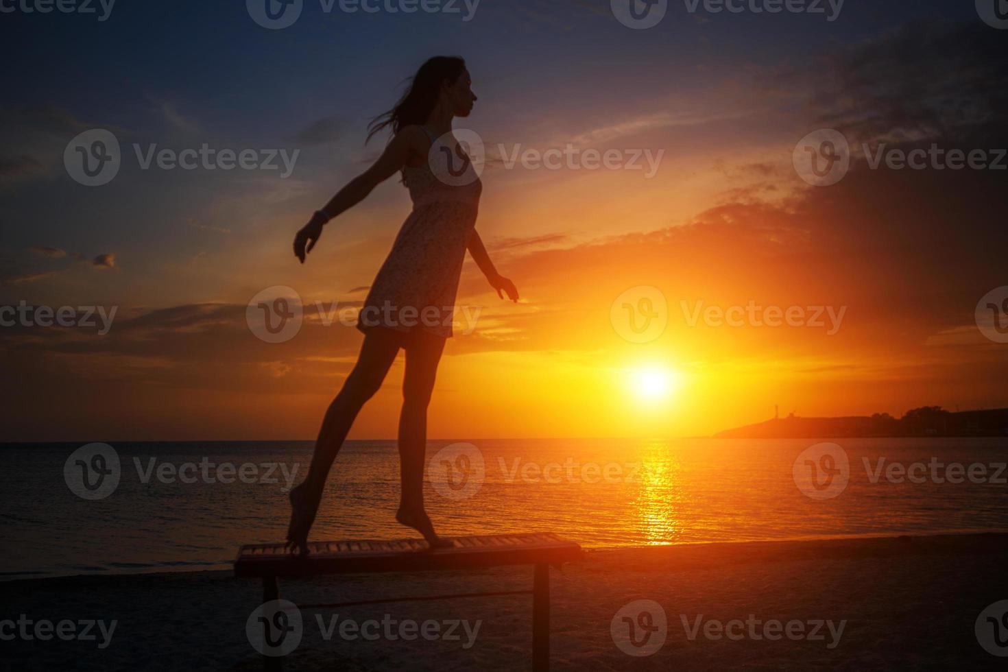 bella joven esbelta parada en la playa al atardecer, hermosa silueta contra el cielo foto