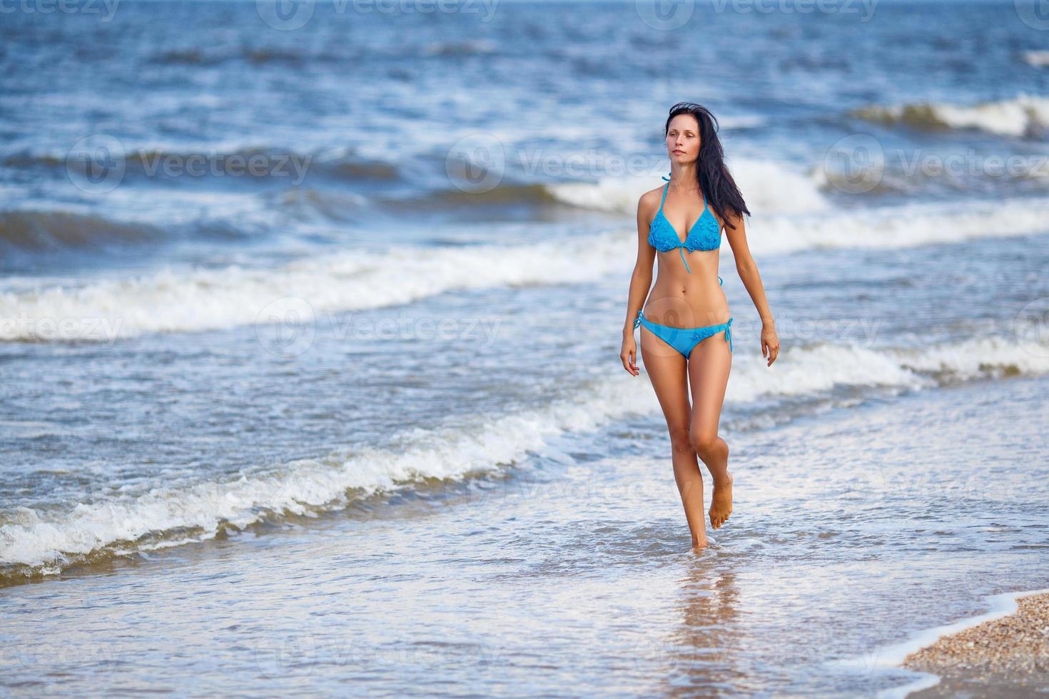 beautiful slender woman in a blue swimsuit walking on the beach photo