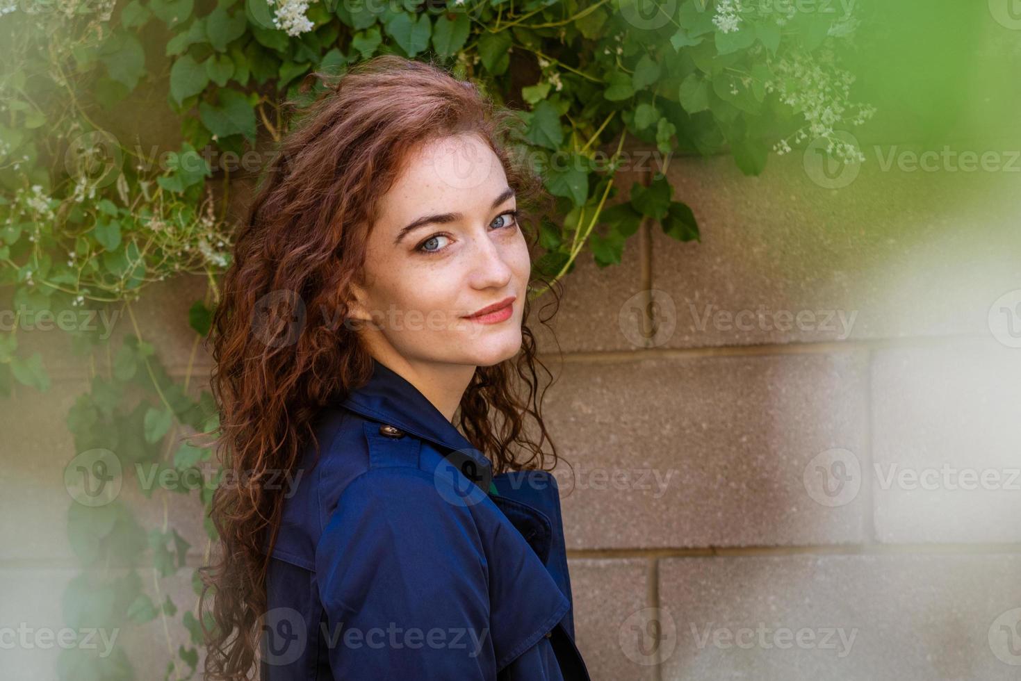 beautiful young woman with red hair and freckles on background of wall photo