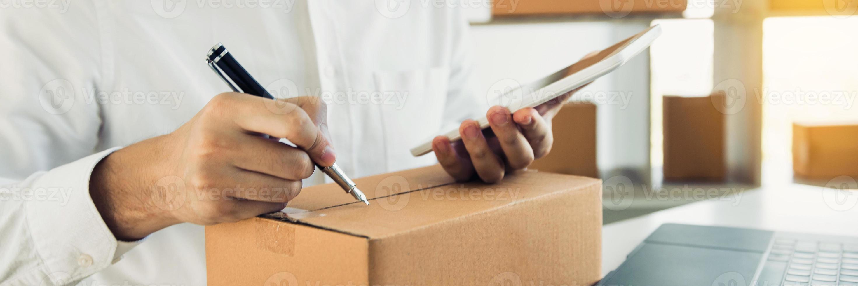 Asian business teenager is looking on tablet and writing a customer address contact to deliver the package to the customer at the destination. photo