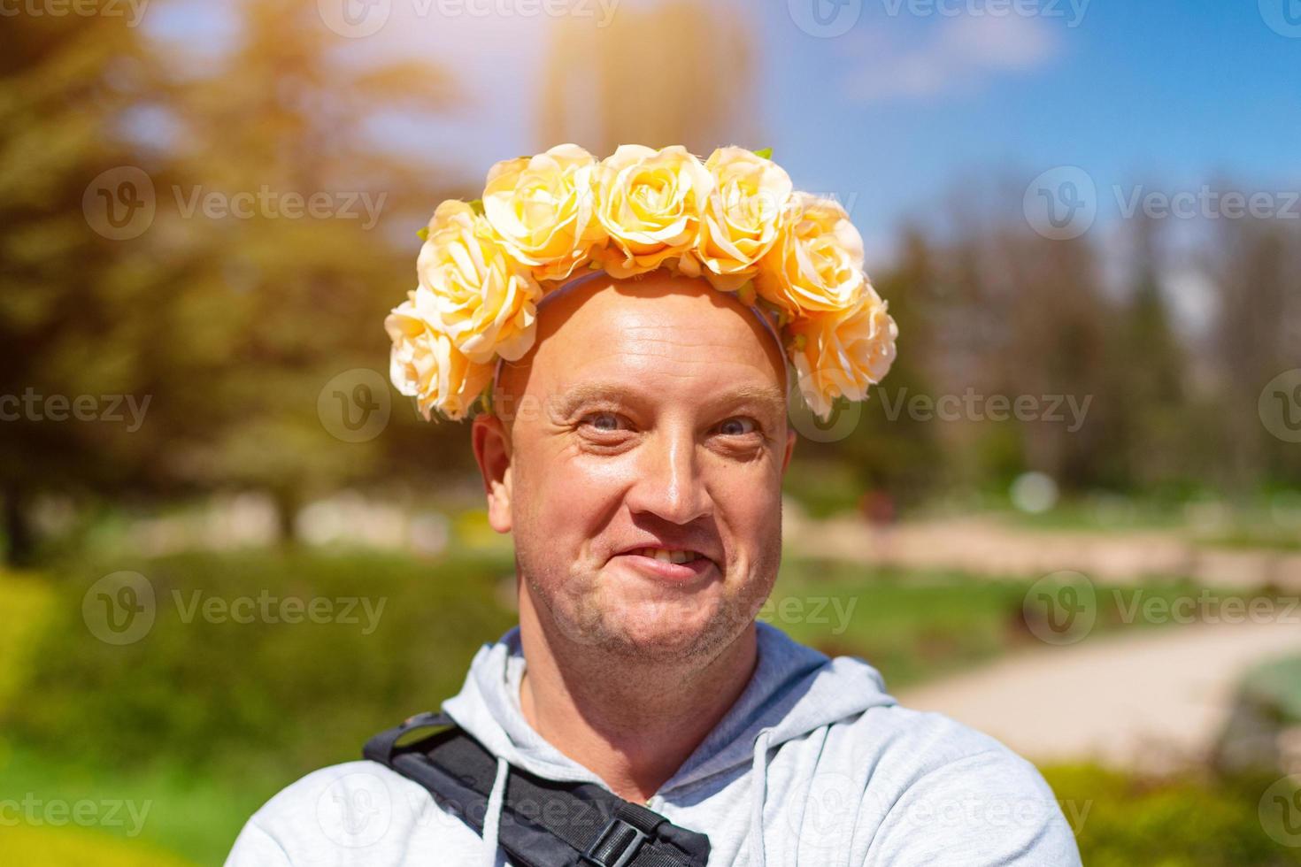 Cheerful portrait of a bald man with a wreath of flowers on his head on a Sunny day photo
