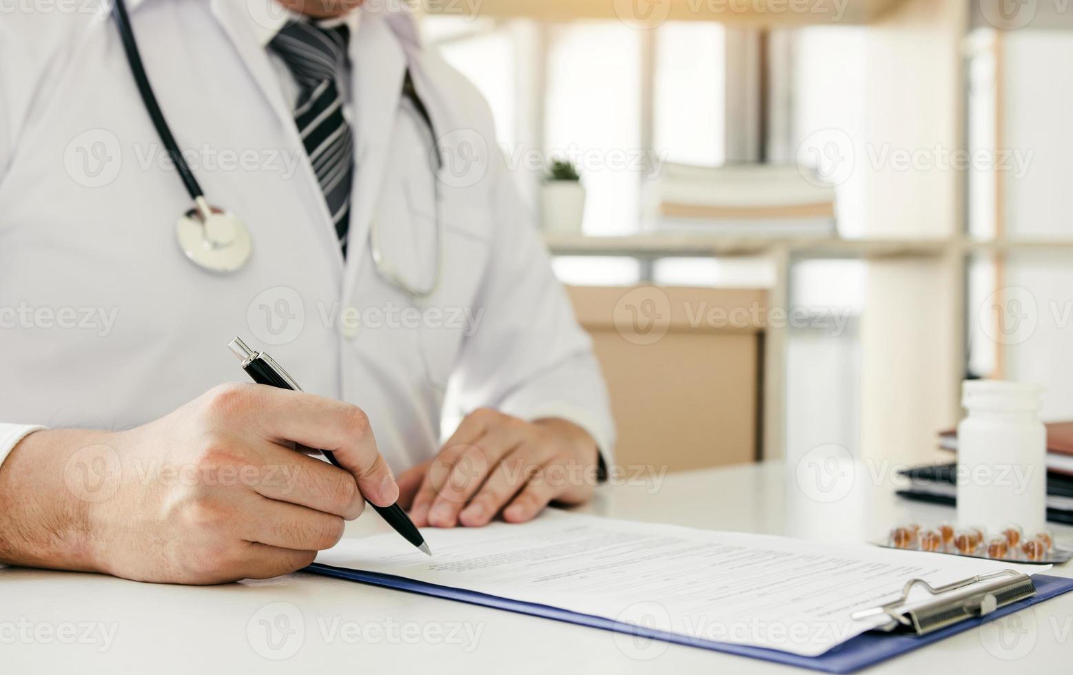 Doctor hand holding pen writing patient history list on note pad and talking to the patient about medication and treatment. photo