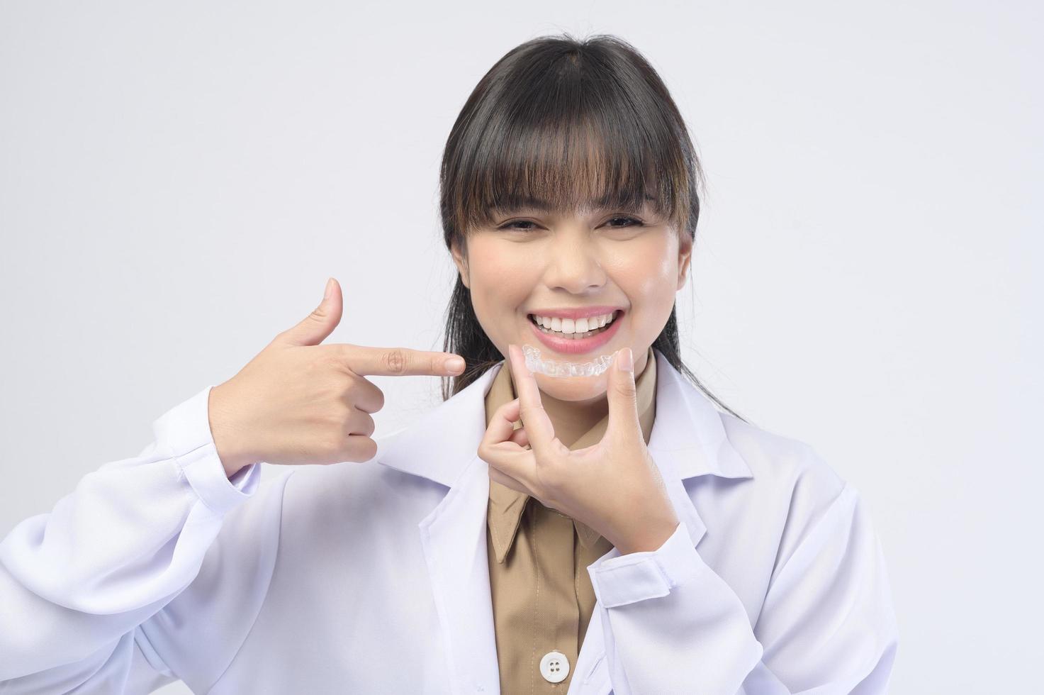 Young female dentist holding invisalign braces over white background studio, dental healthcare and Orthodontic concept. photo