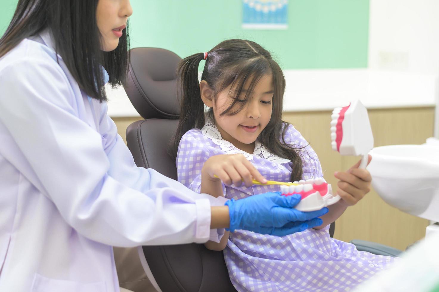 Female dentist demonstrating how to brush teeth to a little girl in dental clinic, teeth check-up and Healthy teeth concept photo