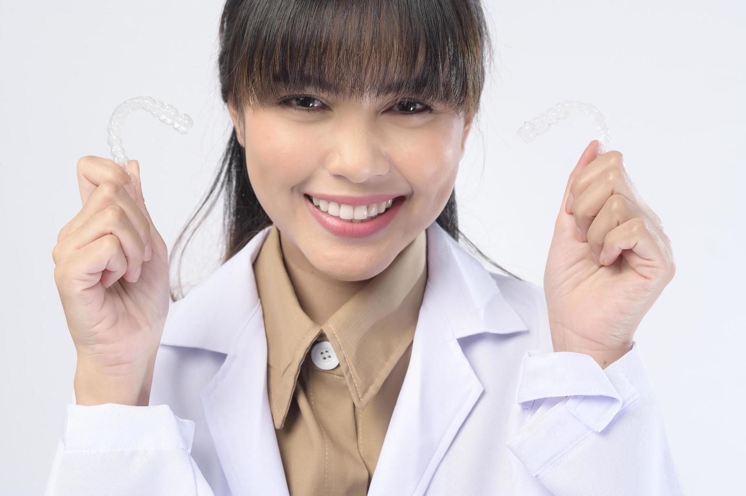 Young female dentist holding invisalign braces over white background studio, dental healthcare and Orthodontic concept. photo