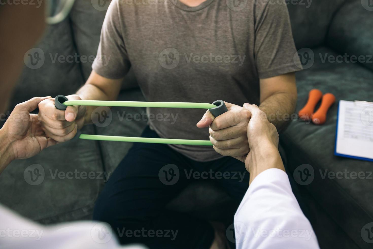 Asian male physical therapist descent working and helping to protect the hands of patients with patient doing stretching exercise with a flexible exercise band in clinic room. photo