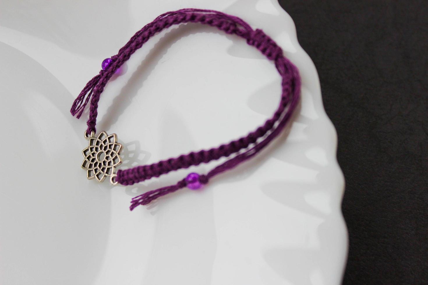 purple braded bracelet with chakra sahasrara on the edge of a snow-white plate photo