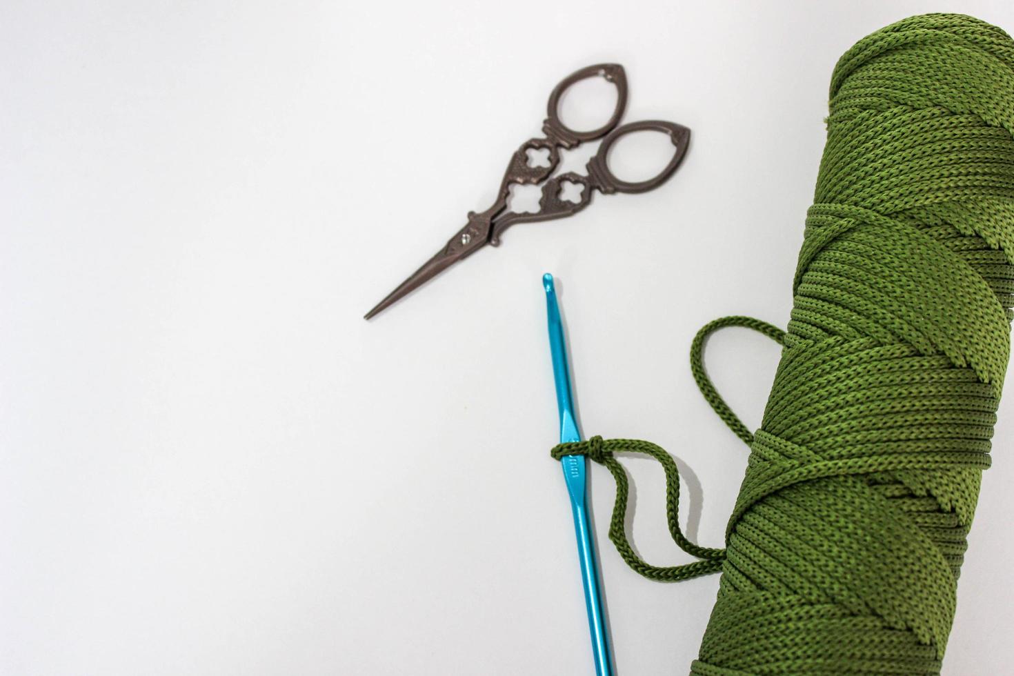 Blue crochet hook and a skein of cord on a white background. On one hook - a loop from the cord, made to start knitting. Vintage scissors are nearby photo