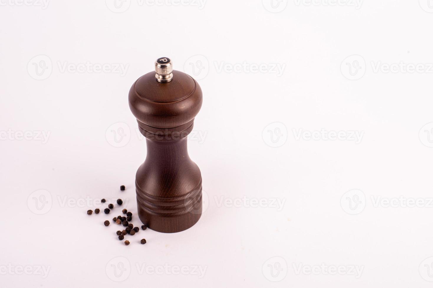 Wooden pepper grinder with pepper on white background. photo