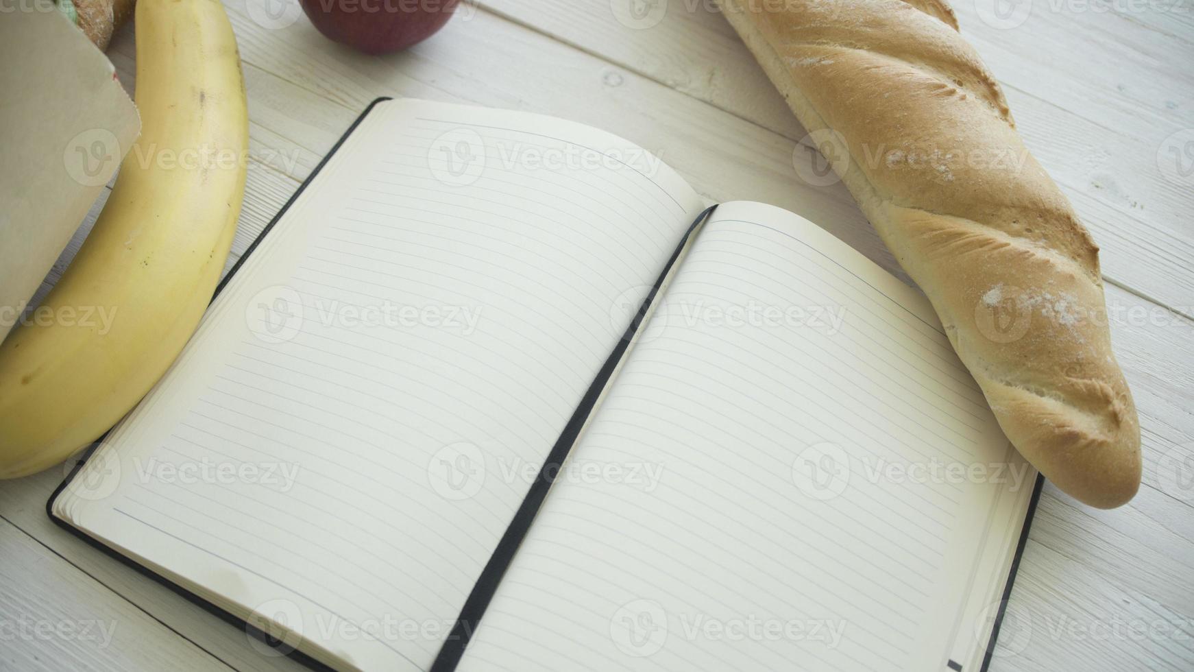 bolsa de papel llena de productos alimenticios con un pequeño cuaderno en blanco sobre una mesa de madera, vista superior foto