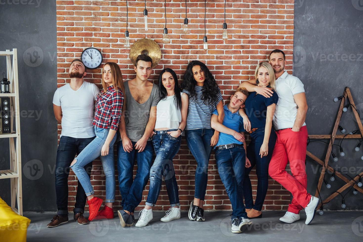 Group portrait of multi-ethnic boys and girls with colorful fashionable clothes holding friend posing on a brick wall, Urban style people having fun, Concepts about youth togetherness lifestyle photo