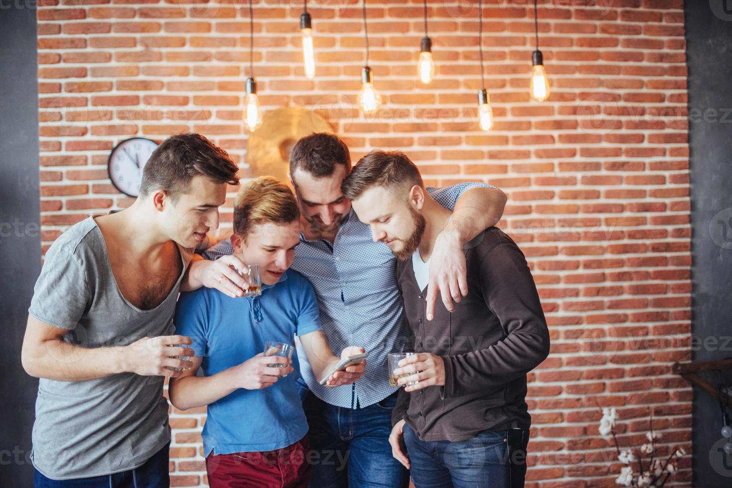 Cheerful old friends communicate with each other and phone watch,  glasses of whiskey in pub. Concept  entertainment  lifestyle. Wifi connected people in bar table meeting photo