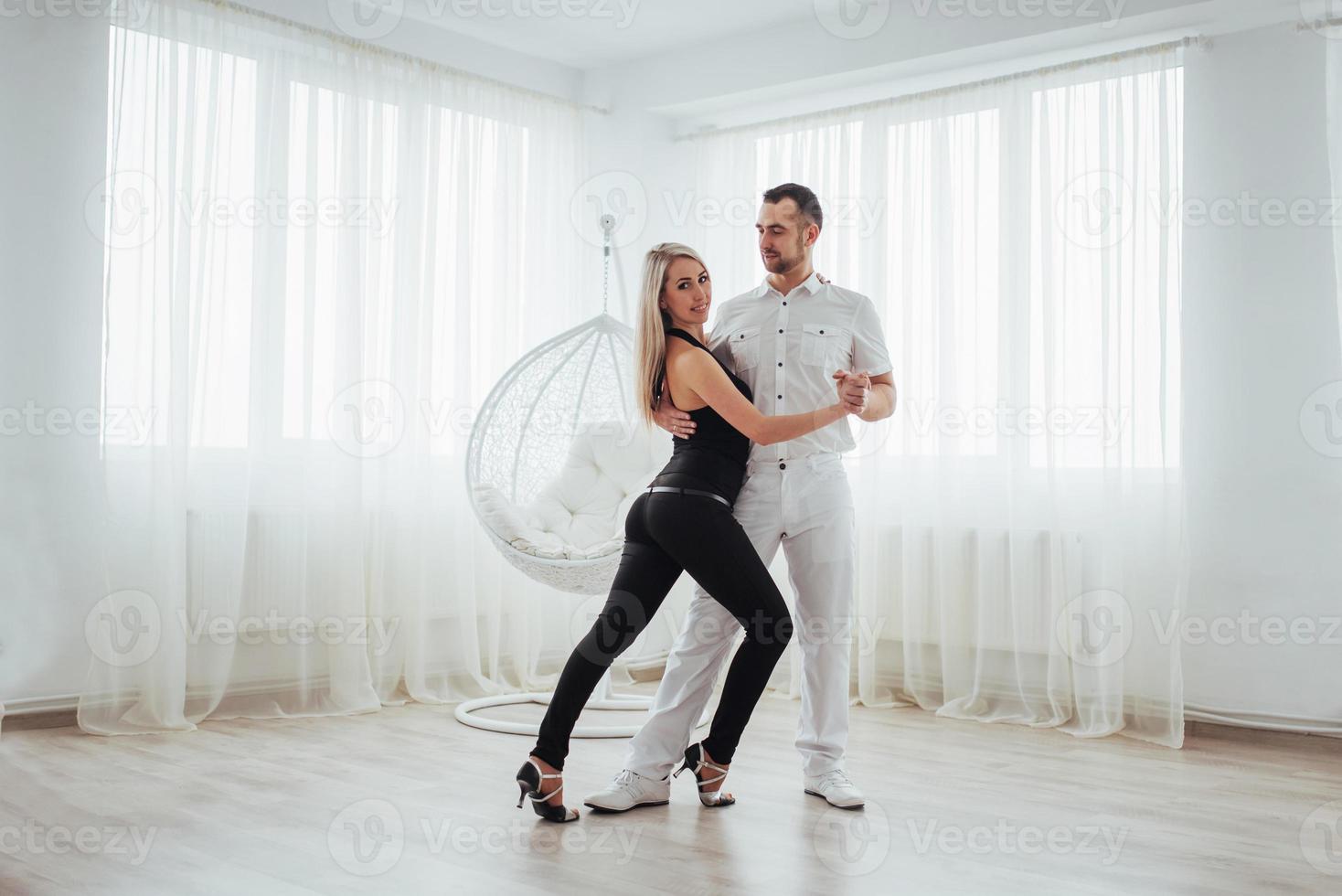 pareja joven bailando música latina bachata, merengue, salsa. pose de dos elegancia en la habitación blanca foto