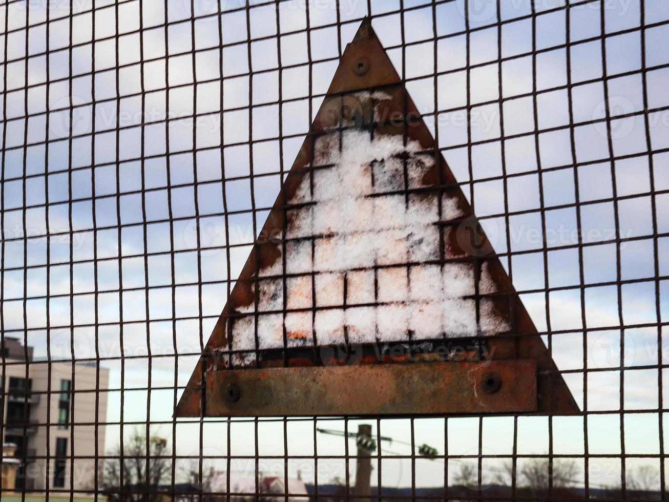 Warning sign rusty back with stuck snow on wire fence photo