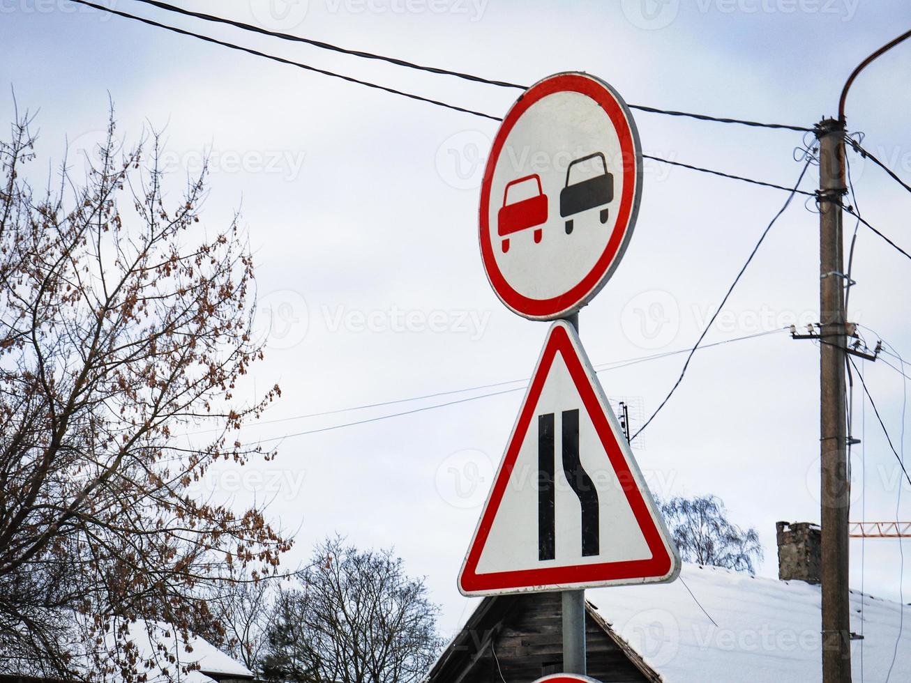 Road signs no overtaking round signa and triangle on sky background with leafless trees and snowy rooftop photo