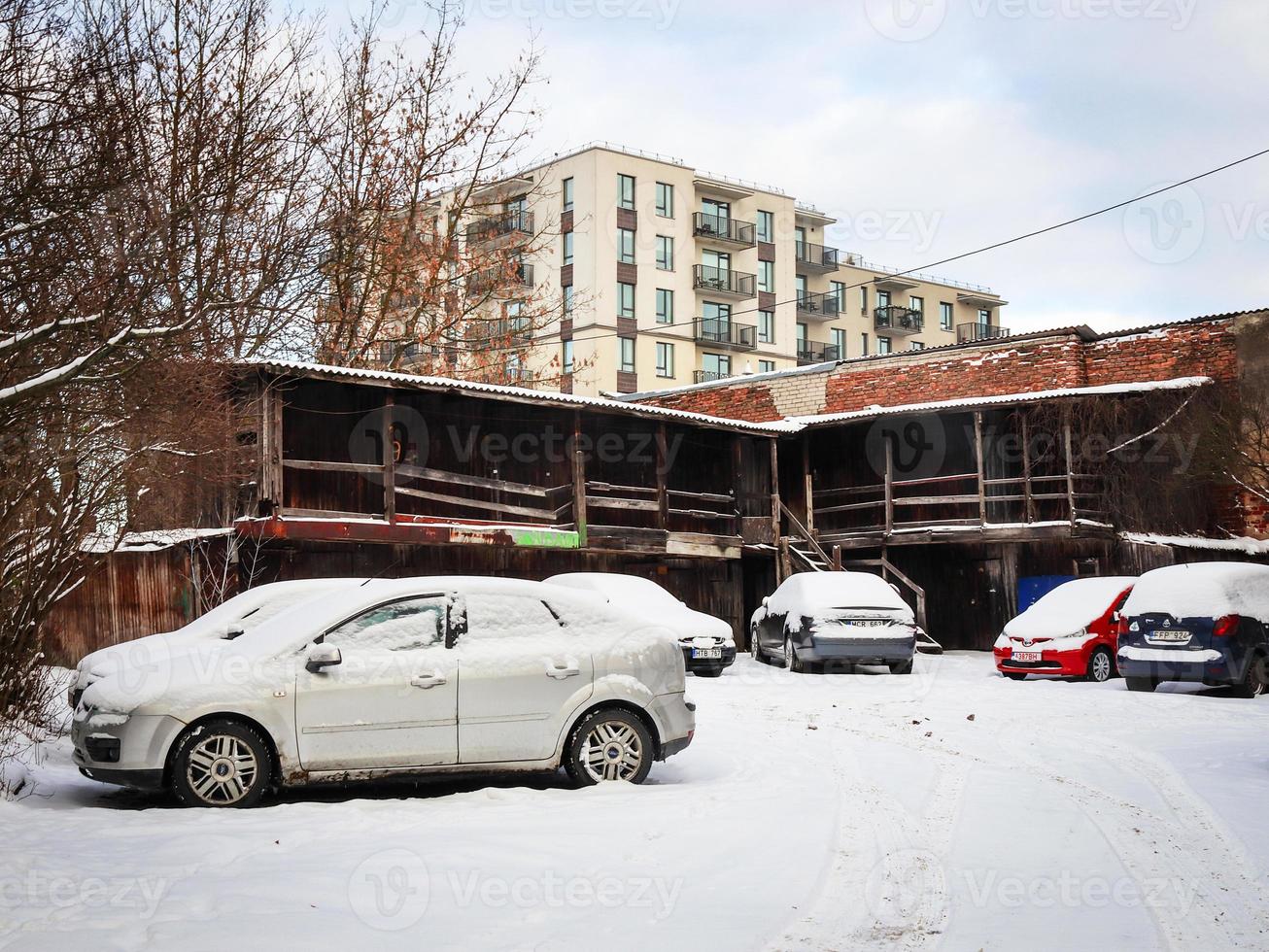 Old weathered storage shed on modern newly built building and parking with cars in winter photo
