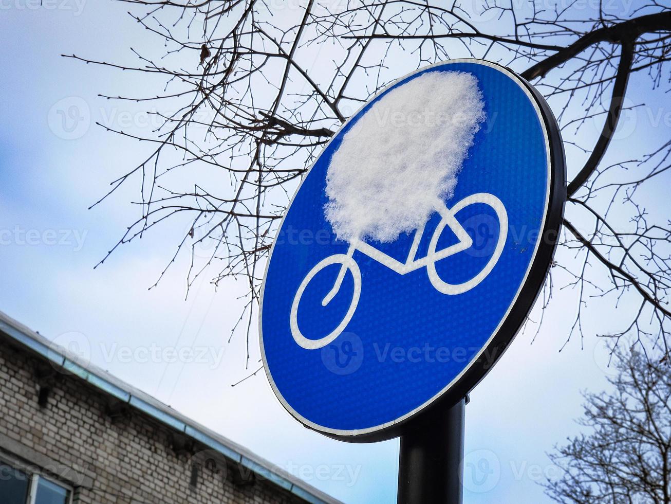 Señal de carretera de bicicleta redonda azul con gota de nieve en ramas de árboles sin hojas y fondo del cielo foto