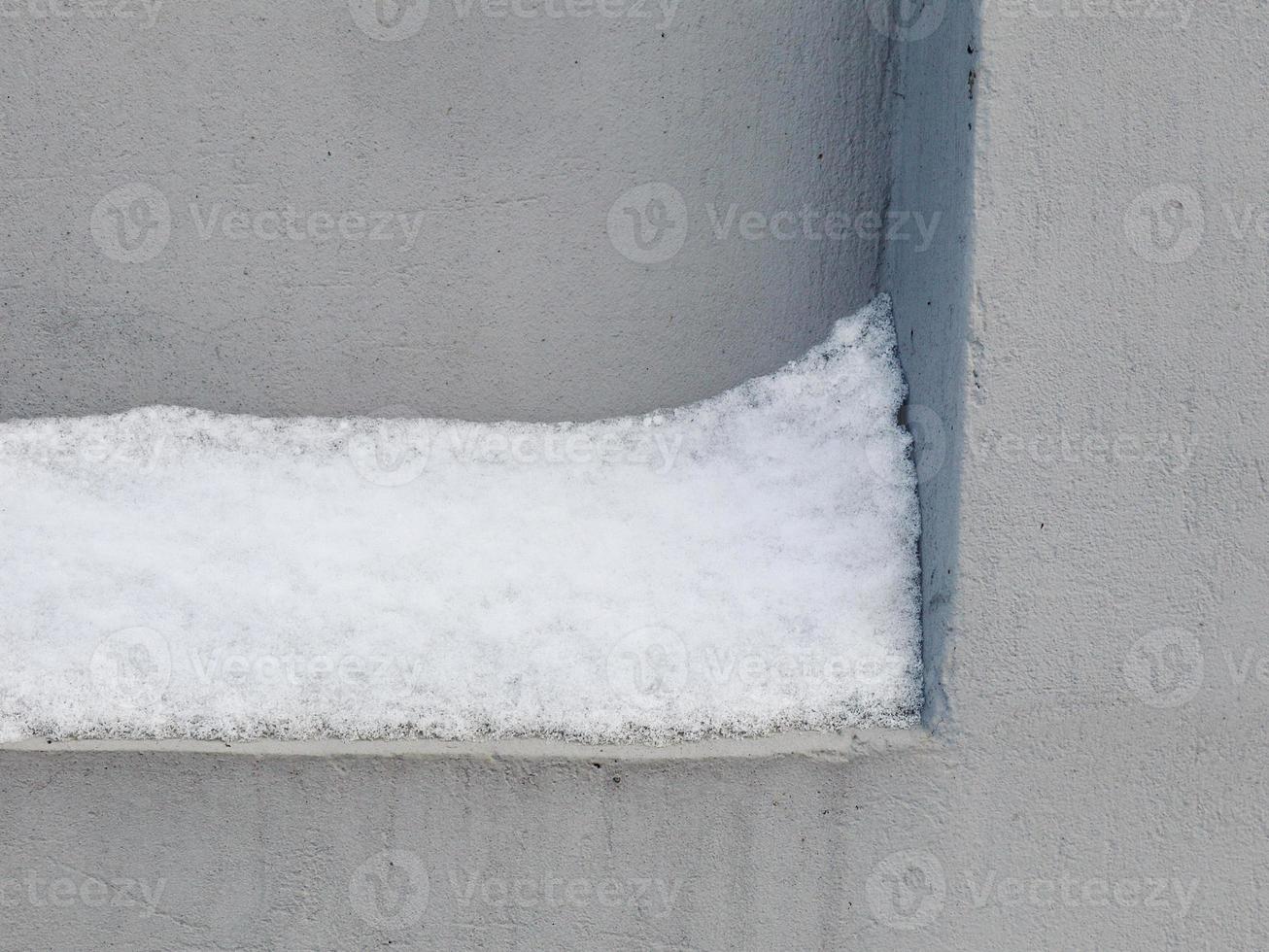 Snow layer stuck on concrete indent in gray cold wall photo