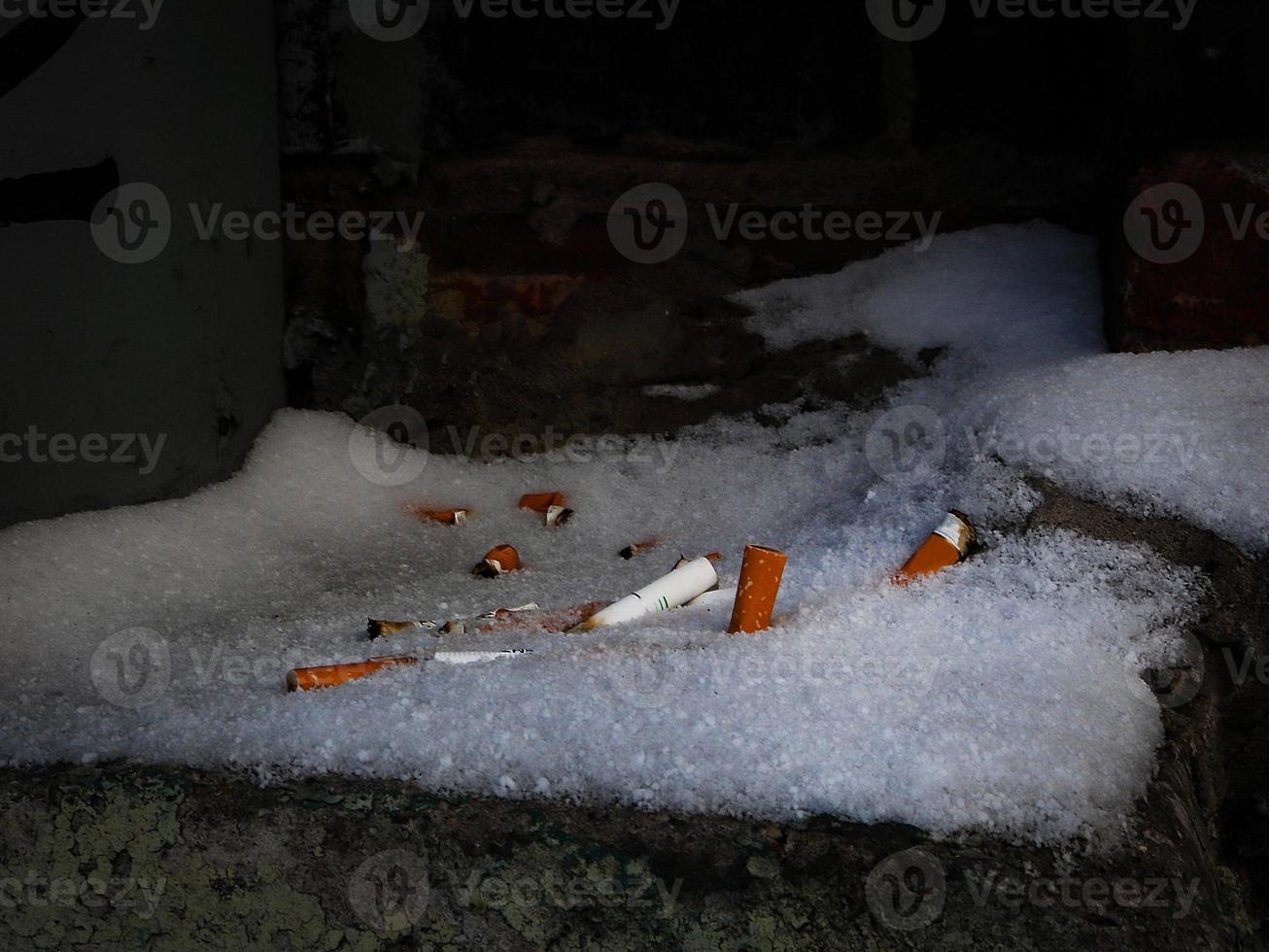 colillas de cigarrillos dejadas en la nieve escondidas en un rincón oscuro foto