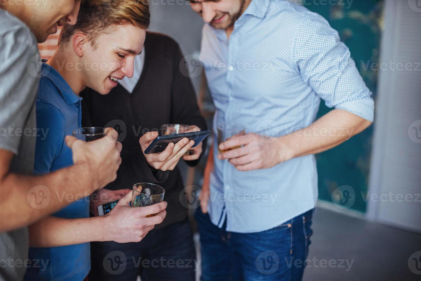 viejos amigos alegres se comunican entre sí y miran por teléfono, vasos de whisky en el pub. concepto de estilo de vida de entretenimiento. personas conectadas wifi en una reunión de mesa de bar foto