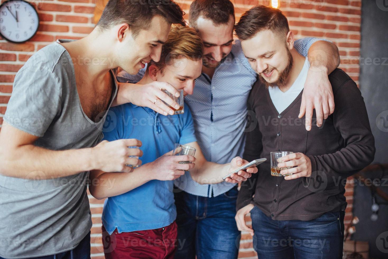 Cheerful old friends communicate with each other and phone watch,  glasses of whiskey in pub. Concept  entertainment  lifestyle. Wifi connected people in bar table meeting photo