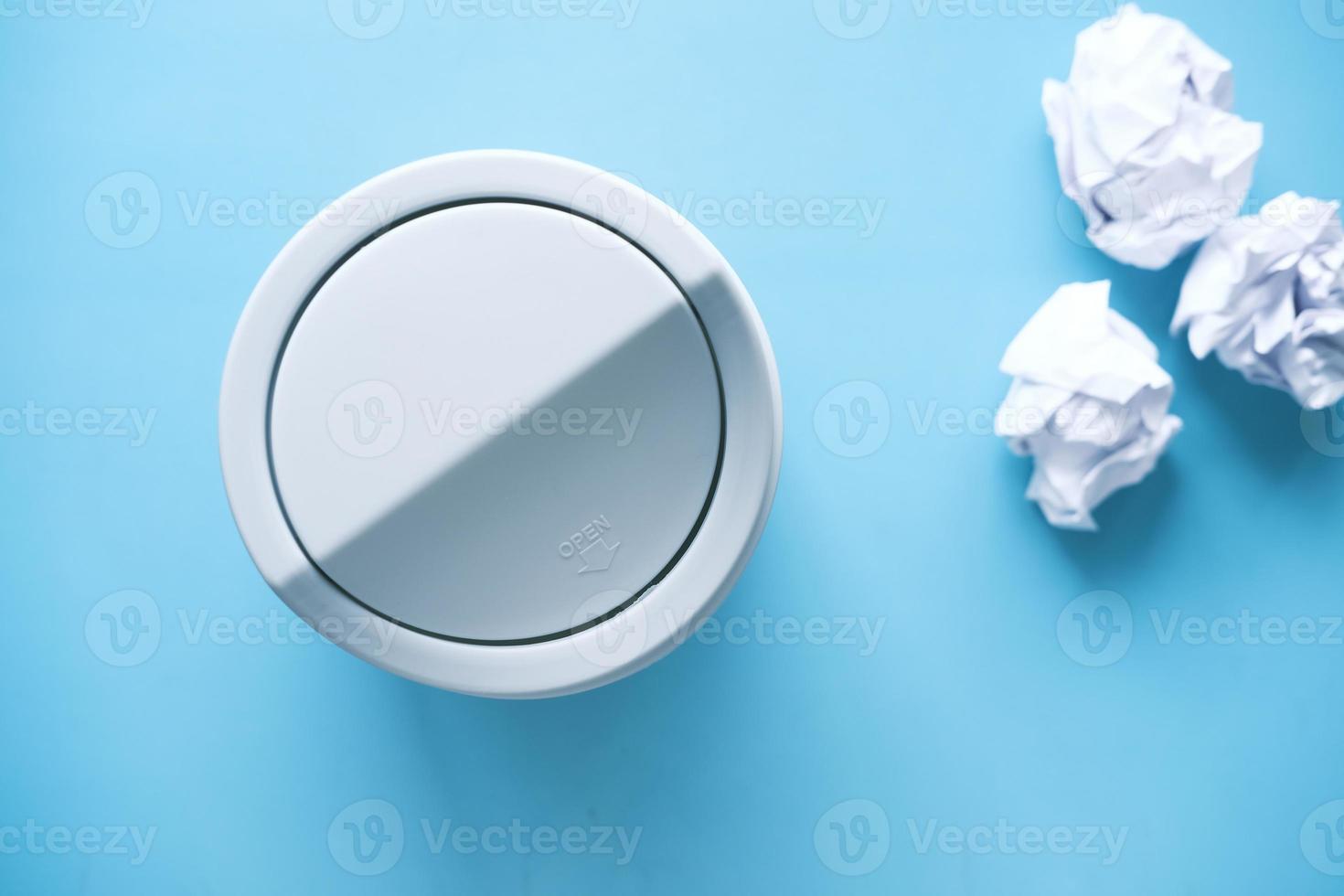 crumpled paper ball in a bin on blue background top view photo