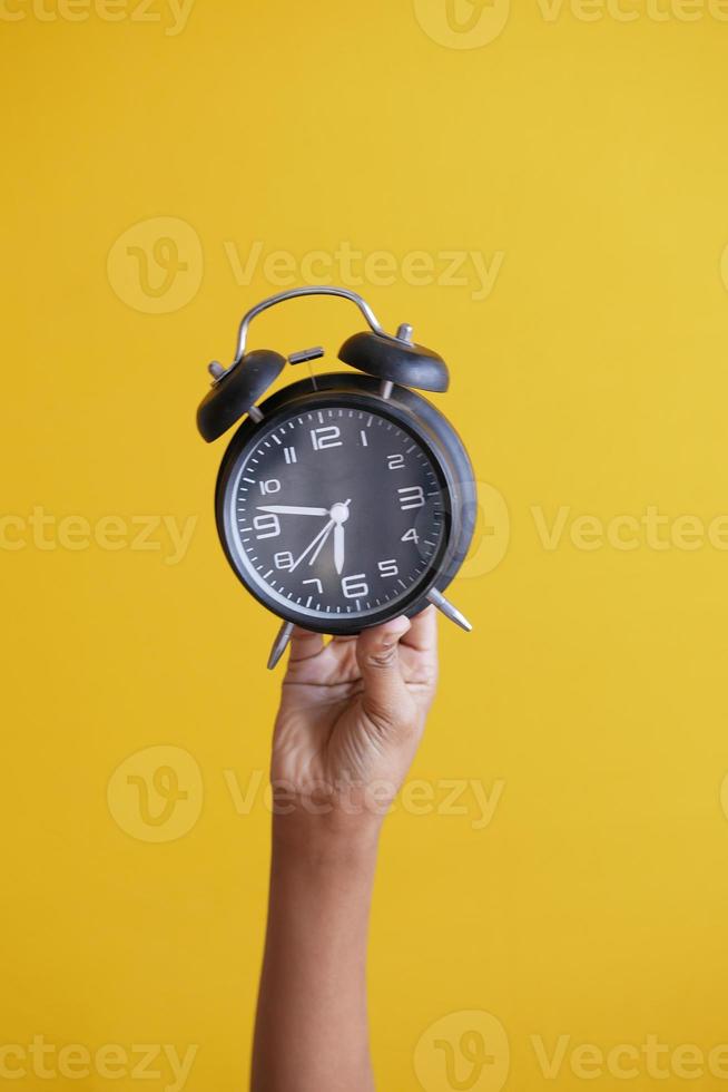 person hand holding alarm clock on yellow background , photo