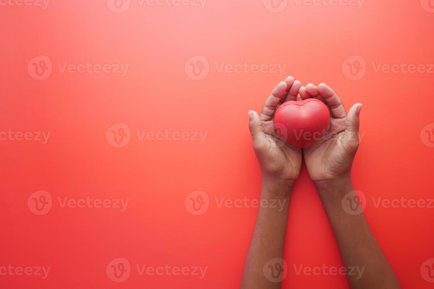 man hand in protective gloves holding red heart on blue photo