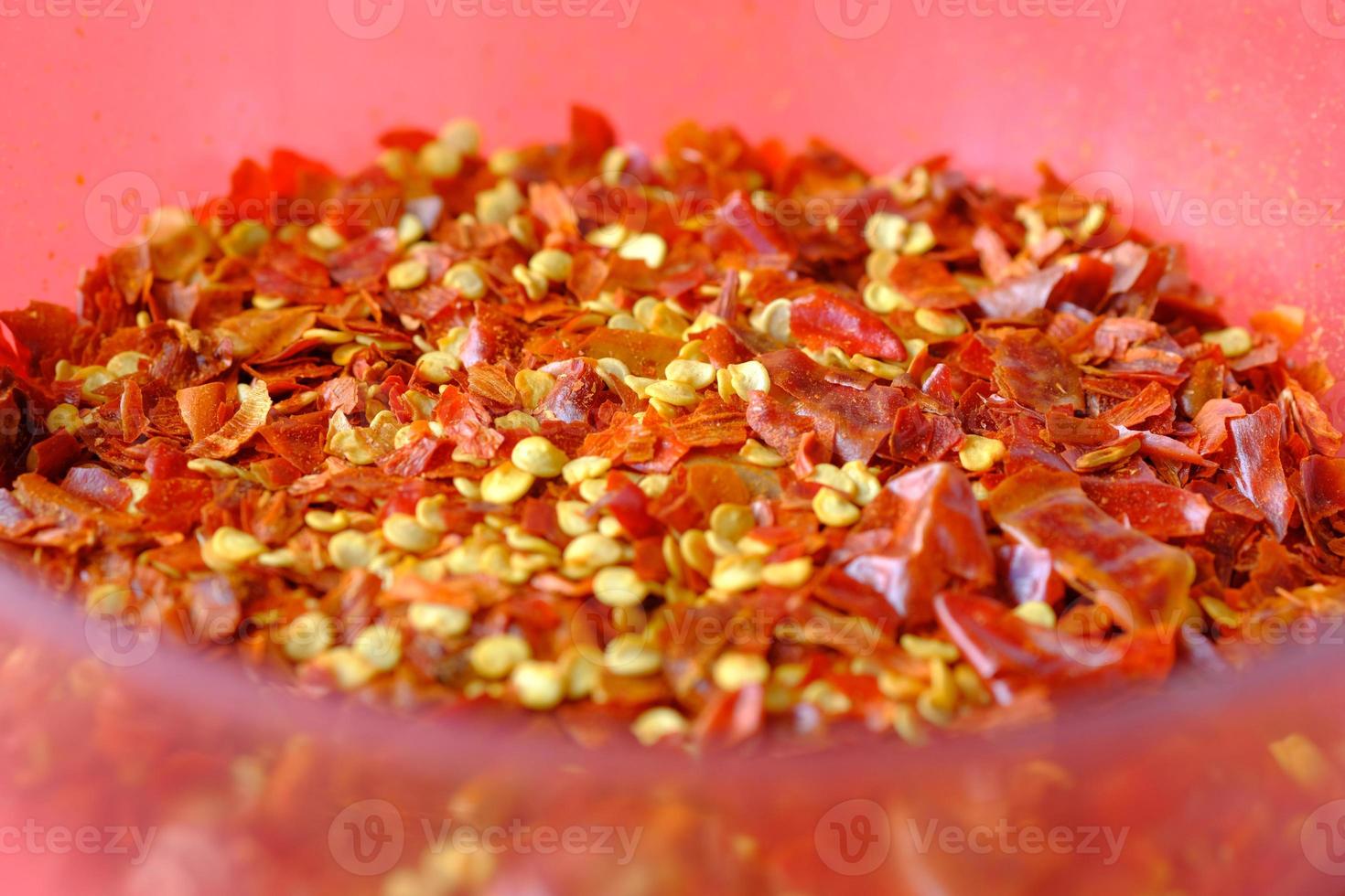 close up of red chili flakes in a bowl on red photo
