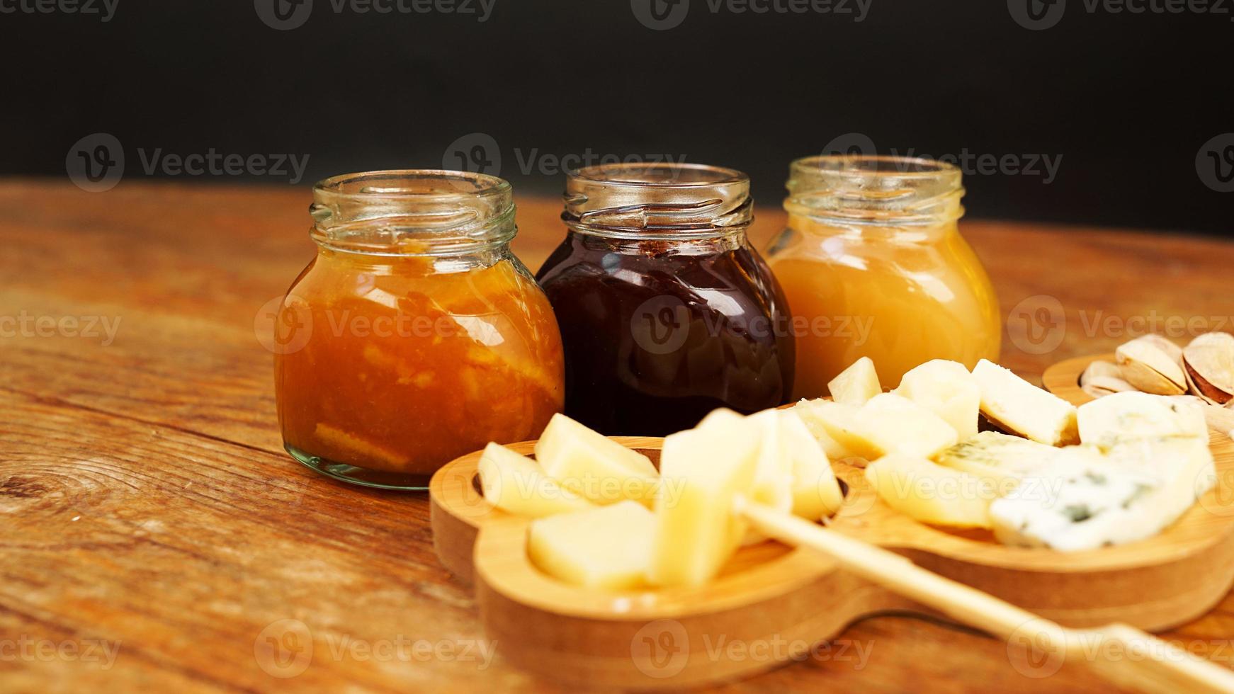 Jars of homemade jams and a variety of cheeses on a wooden table. Cheese plate photo