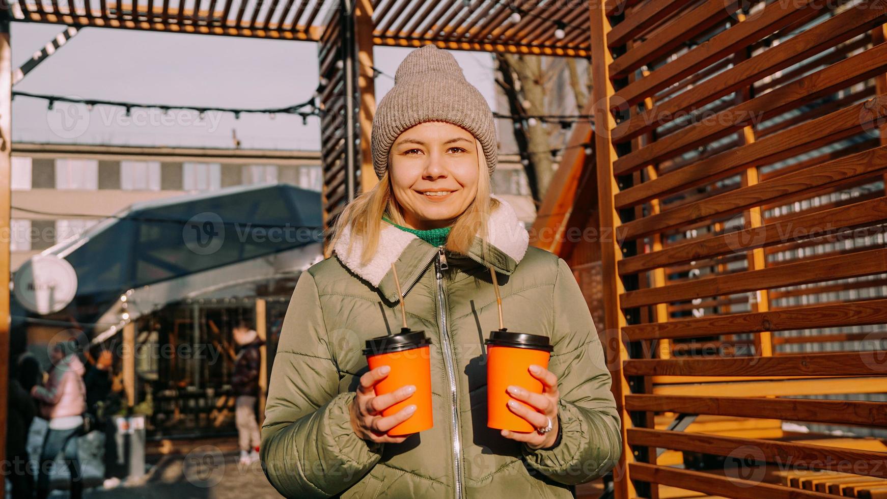 Woman carries two cups of coffee or mulled wine at the city outside food court photo