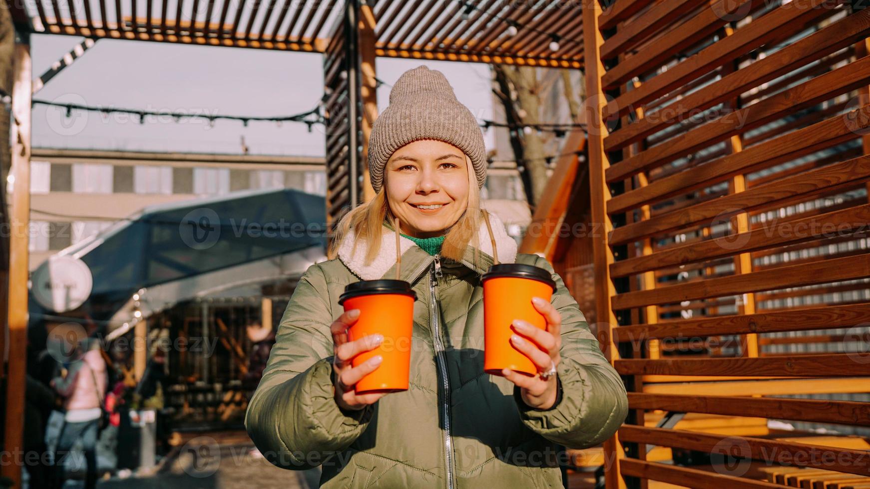 mujer lleva dos tazas de café o vino caliente en la ciudad fuera del patio de comidas foto