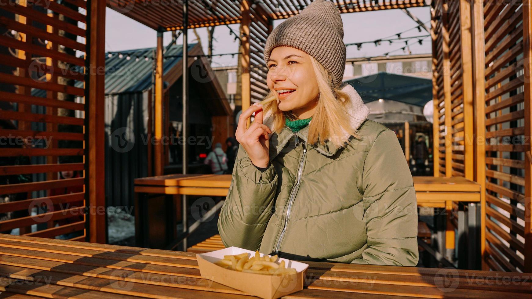 Woman eating tasty french fries in outdoor cafe. Sunny winter day photo